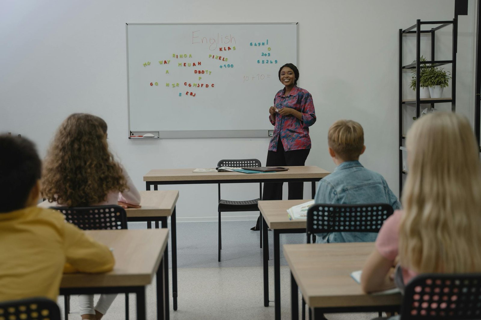 A diverse group of students in an English class with a smiling teacher at the whiteboard.